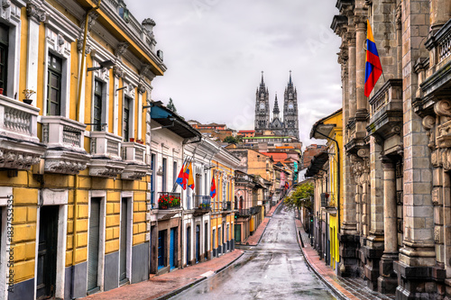 Cobblestone street leads toward Basilica del Voto Nacional in Quito, Ecuador. Historic center landscape features colonial buildings and wet road under cloudy sky in UNESCO World Heritage site