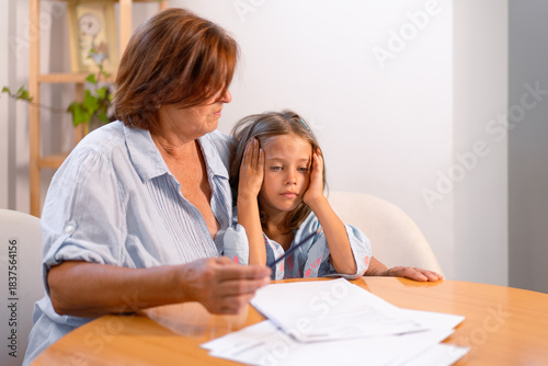 Little girl feel unmotivated to do prepare homework with grandmother at table. Caring grandparent studying with small girl child at home, education, school problem concept