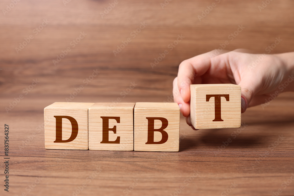 Naklejka premium Woman making word Debt of cubes with letters on wooden table, closeup
