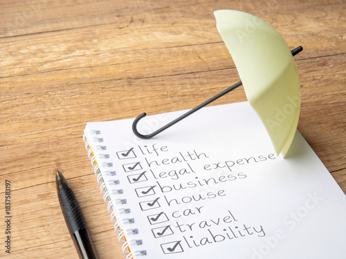 Checklist of various insurance categories on a notebook with a small umbrella. Protection, coverage, risk management, and financial security concept.
