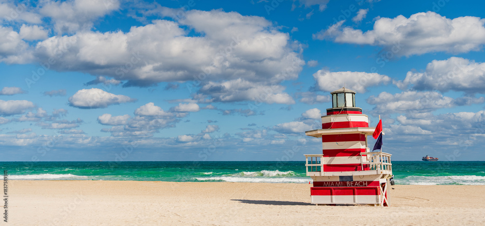 Fototapeta premium Lifeguard tower on the sandy Miami Beach shore. Iconic Art Deco lifeguard station under summer sky. Scenic view of South Beach coastline in Florida. Colorful lifeguard tower, symbol of Miami tourism.