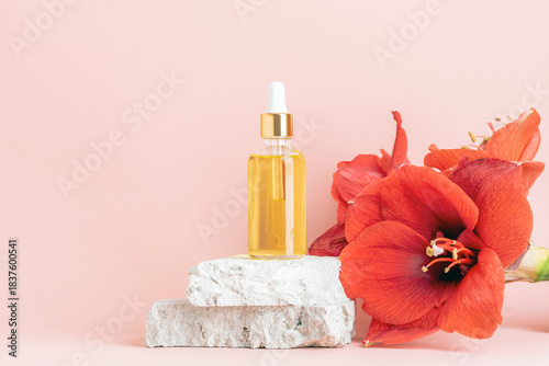 Glass serum bottle on stone blocks beside red amaryllis flowers on soft pink background. Copy space
