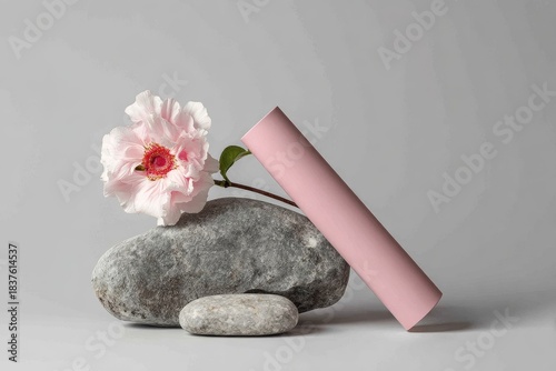 Pink cylinder leans on grey stones and a pink flower