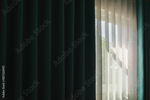 Fotografija Morning sunlight filtering through sheer curtains beside dark drapes