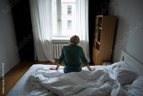 Dressed middle aged woman sits on bed in bedroom unmotivated to get up, body pose showing heavy depression and life crisis. Female in deep thinking about feelings and emotions, dealing with drama.