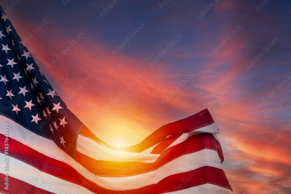 Obraz premium American flag waving with sunlight glowing through stripes against dramatic colorful sky symbolizing pride and freedom
