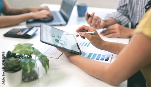 Close-up of a businesswoman typing on a laptop displaying financial data and charts during a team meeting.