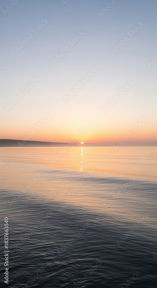 Fototapeta premium Distant sun reflects upon calm water surface during soft twilight