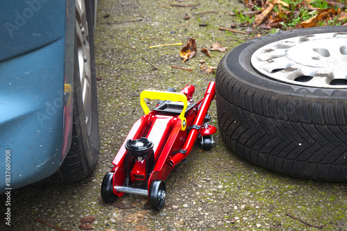 Changing a flat tire with a red jack and spare tire on the side of the road