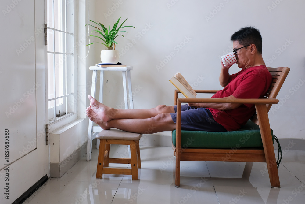Obraz premium man sitting alone on armchair reading a book at weekend