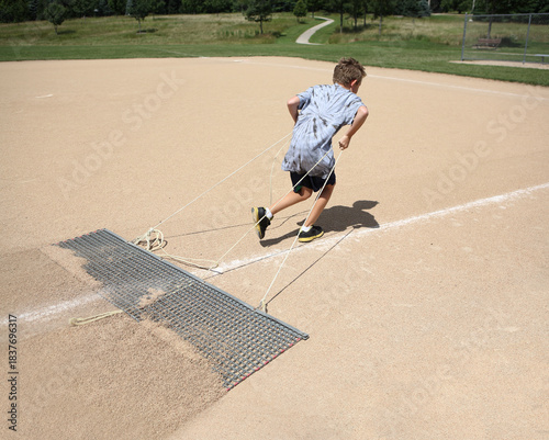 Young boy pulling an infield drag grooming the field for a baseball game