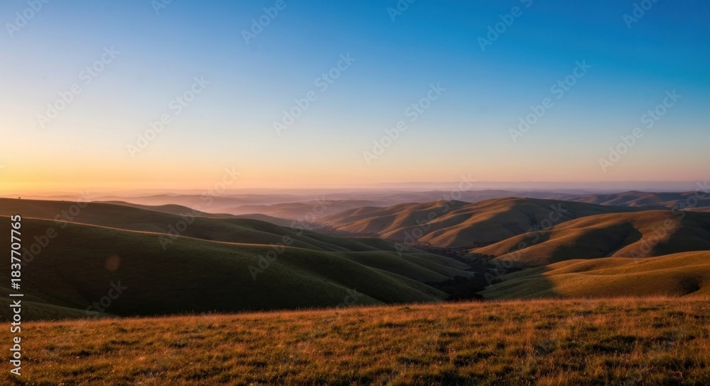 Fototapeta premium Sunrise over rolling hills. Vast landscape bathed in golden light. Soft, hazy atmosphere. Distant valleys