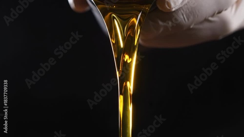 Closeup of golden viscous liquid, possibly oil or honey, being poured from a container by a hand wearing a white glove