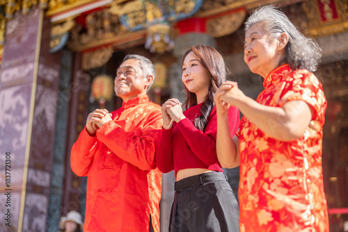Asian family in red clothes making traditional Chinese New Year greeting gesture at temple, celebrating lunar new year with respect and joy, showing multigenerational and festive cultural appreciation