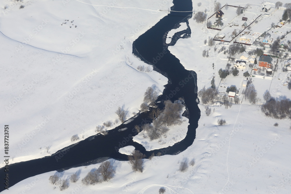 Fototapeta premium Aerial view of winding river surrounded by snow-covered landscape