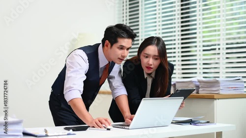 Two  Asian businessman and woman workers talking on the smartphone and using laptop Professionals in Teamwork Finance, Marketing, and Success at the office.