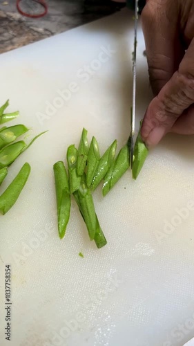 Hand movement of a bean cutter with a sharp knife on a white chopping board