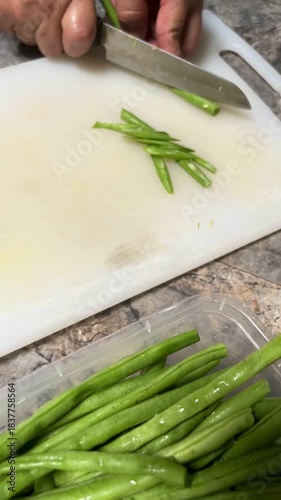Hand movement of a bean cutter with a sharp knife on a white chopping board