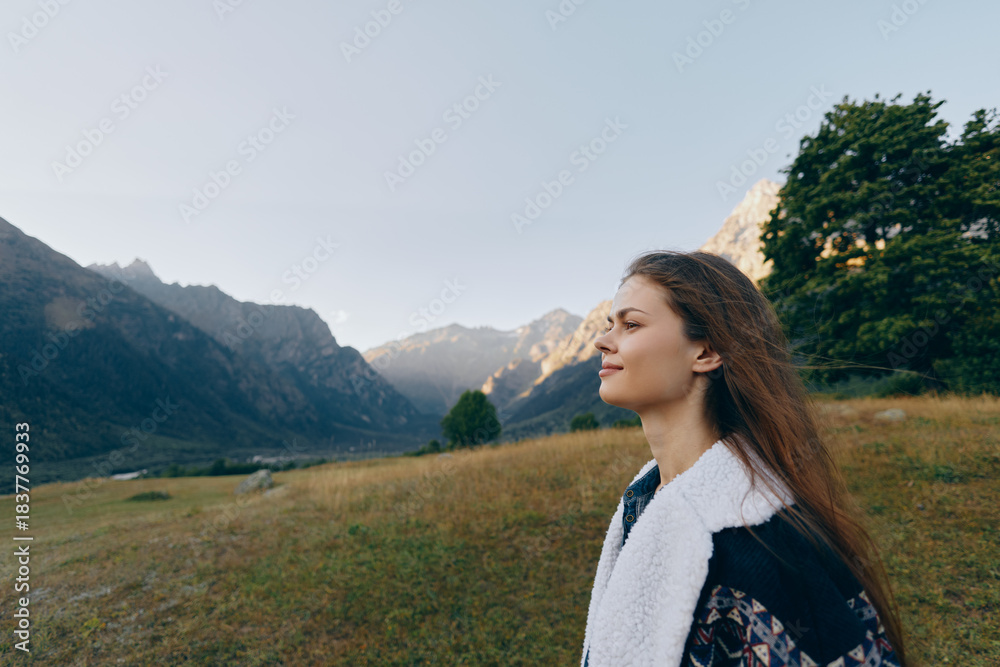 Obraz premium Woman profile portrait in mountains meadow, outdoors and contemplative with trees and distant peaks. Nature scene with calm expression, layered jacket and soft light over grassland.