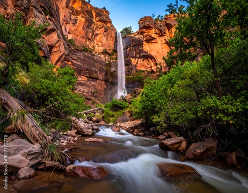 Waterfall cascades down cliff face into flowing stream surrounded by foliage