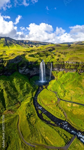 Waterfall cascades down cliffs into a lush green valley under blue sky