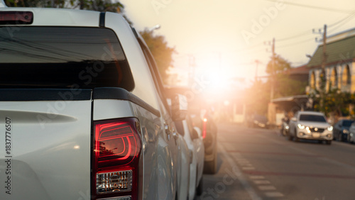 Side of pickup car parking beside road. Dim light of a warm evening. Other car driving on clear road. City and buildings along the road. Under light and evening sky.