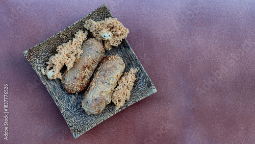 Above view of Khao Mao dessert or name Pounded Unripe Rice or Shredded Rice Grain. Dish made from ripe bananas wrapped in rice and fried. Placed on a wooden plate on a light orange tiled floor.