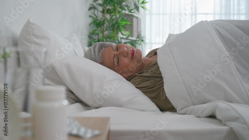 Asian frustrated insomnia senior woman lying down on bed in bedroom. 