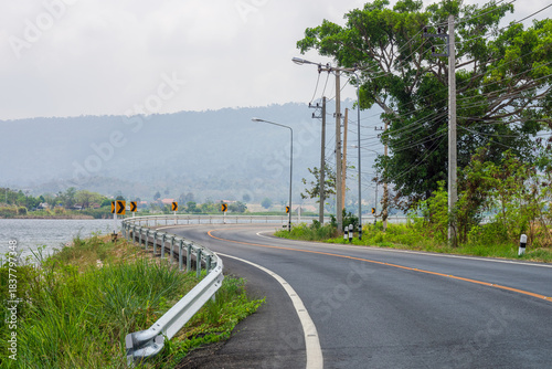 Scenic Curvy Road with Guard Rail at Ban San Kamphaeng Reservoir, Thailand. Road with a silver guard rail and safety chevrons running alongside Ban San Kamphaeng Reservoir in Nakhon Ratchasima.