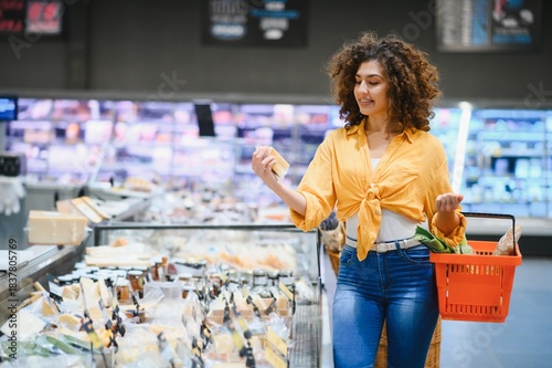 Obraz na plátně Woman choosing cheese in a supermarket deli section