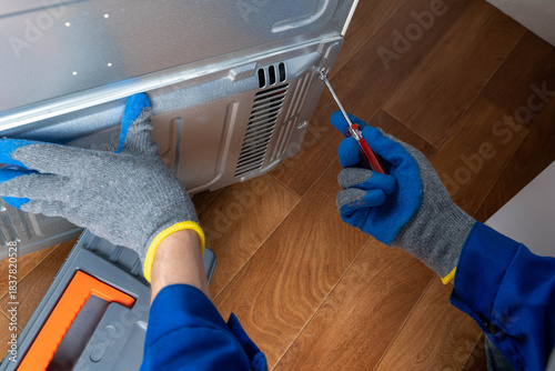 Photography Person repairs kitchen appliance with screwdriver while wearing gloves in home