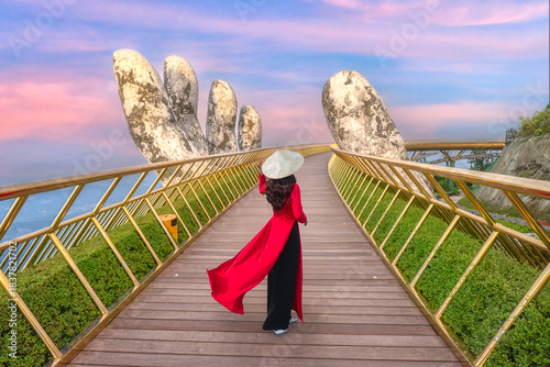 A Vietnamese woman in traditional Vietnamese costume on the Golden Bridge with giant hands, a popular scenic spot and tourist attraction in Ba Na Hills Resort, Da Nang, Vietnam.