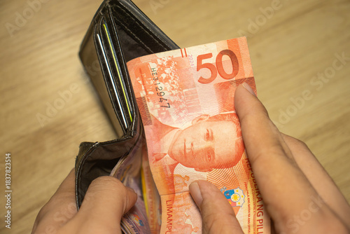 Obraz na płótnie A fifty Philippine peso banknote is being pulled from a black wallet by a pair of hands