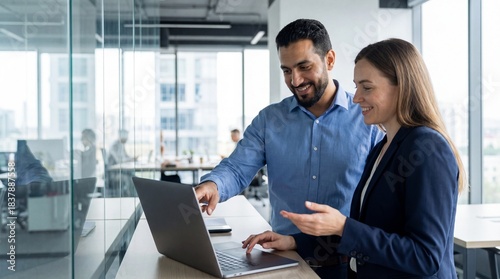Diverse male and female colleagues collaborating on a project using a laptop in a modern corporate office, smiling and discussing.