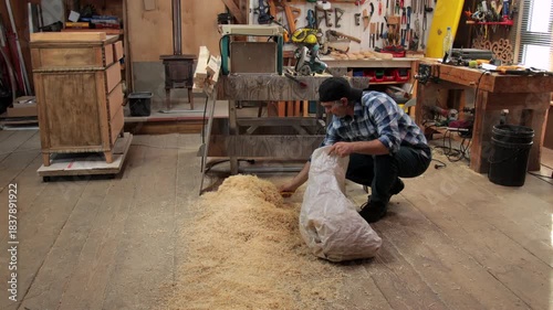 A carpenter collects fresh wood shavings from the floor