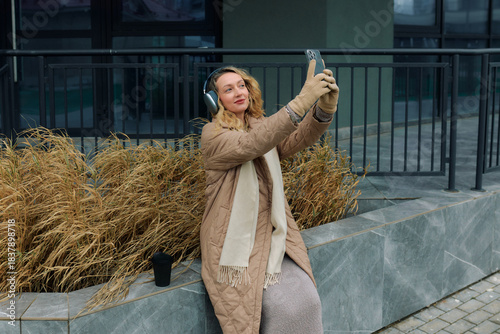Woman enjoys a moment outdoors while taking a selfie and listening to music in a city setting