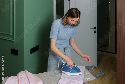Woman ironing a pink striped shirt in a modern home interior during daytime