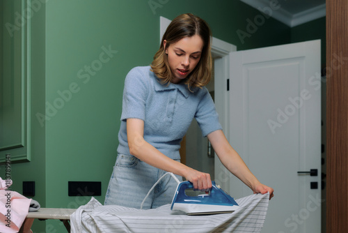 Woman ironing clothes indoors in a stylish room with green walls