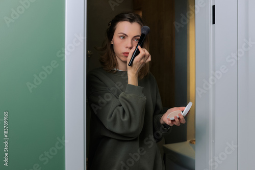 Woman applying makeup in a bathroom, focusing on her beauty routine during the morning hours