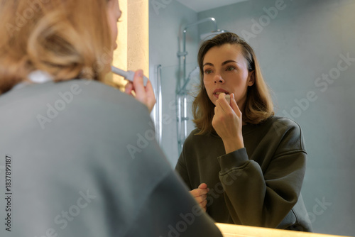 Woman applying lip color in bathroom mirror during morning routine