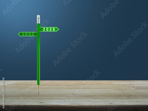 2026 and 2025 direction sign plate with green pencil on wooden table over light blue wall, Business happy new year 2026 planning and strategy concept