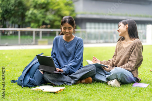 Two asian female students sitting on stairs using laptop for study or project at university, concept of modern education, remote learning, teamwork, digital study and student collaboration knowledge