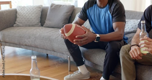 Diverse male friends at home noticing football on coffee table, man rotating ball practicing grip