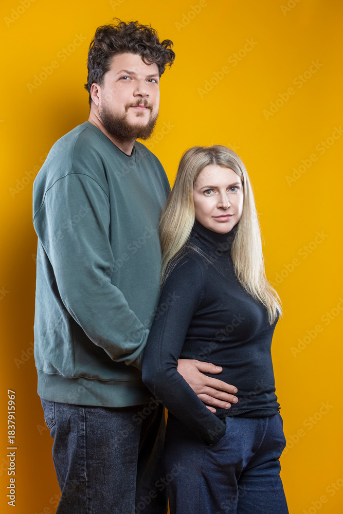 Obraz premium Lifestyle Concepts. Young Positive Caucasian Smiling Happy Adorable Couple As Friendly Family Man And Woman Casual Clothing Together Hugging Embracing Cuddle Isolated on Seamless Yellow Background