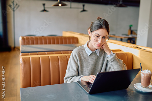 Bild auf Leinwand Young woman wearing glasses focusing on her laptop while telecommuting from a mo