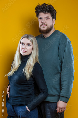 Lifestyle Concepts. Young Caucasian Smiling Happy Adorable Couple As Friendly Family Man And Woman Casual Clothing Together Embracing Cuddle Isolated on Seamless Yellow Background As Studio Portrait.