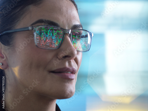 Financial analyst viewing market data on screen with graphs reflecting in glasses