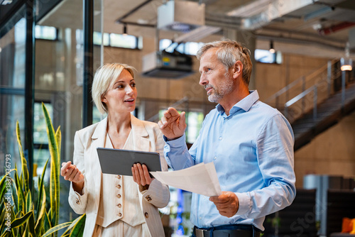 Colleagues discussing business in a modern office holding tablet and papers
