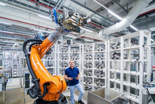 Engineer standing beside industrial robot arm in modern factory