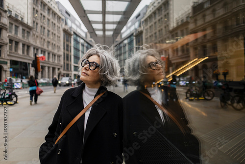 Businesswoman in smart casual looking up with reflection in city street